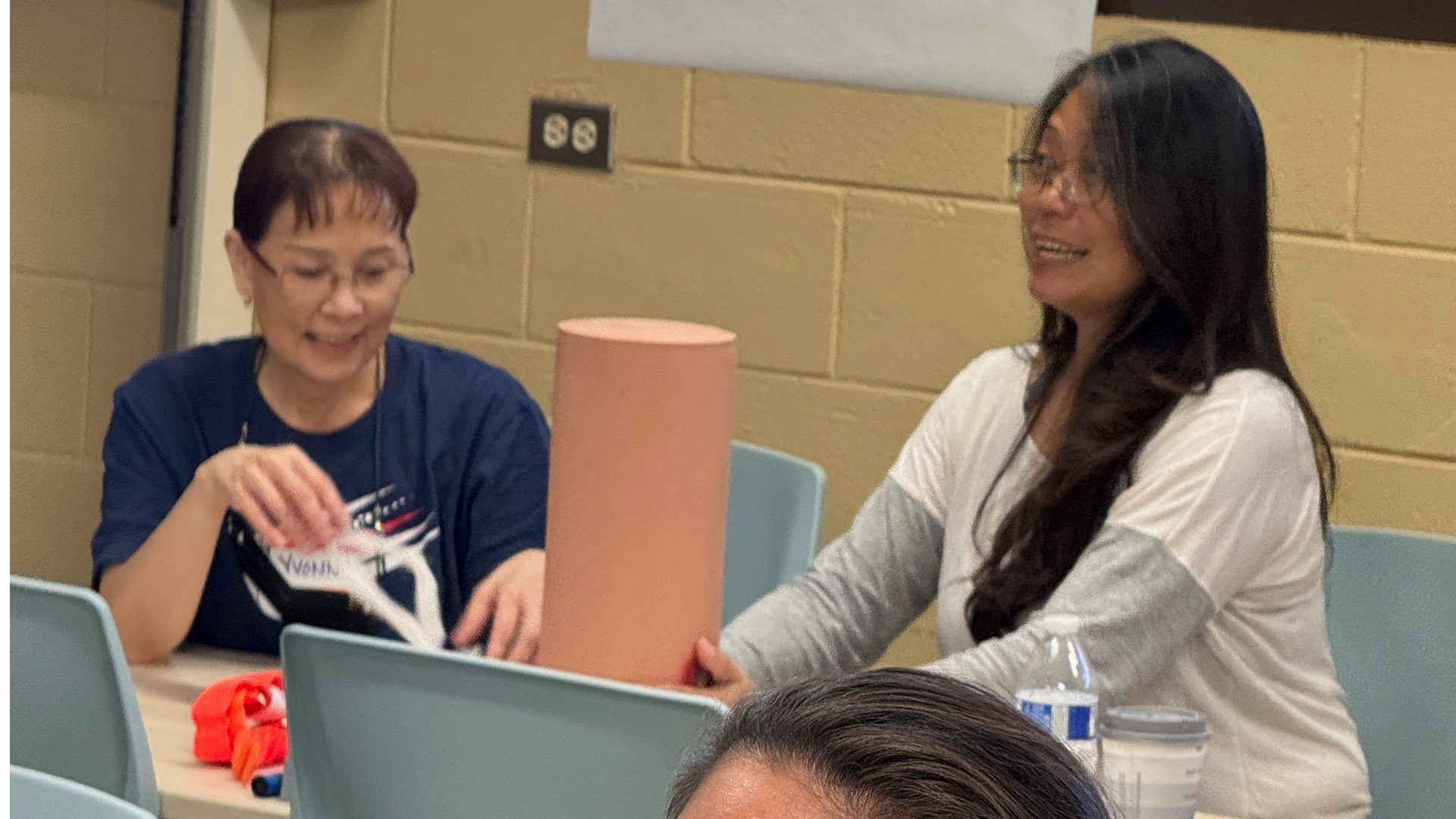 Two women participating in a hands-on activity during a workshop, smiling and engaging with training materials at a table.